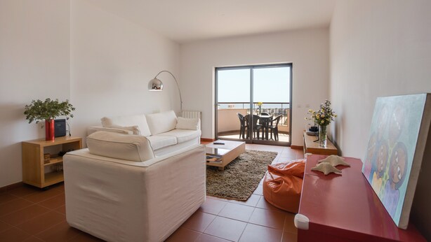 A modern living room with a white sofa, a coffee table, a red accent table, a painting, and a balcony with a dining area. - Apartment "Meia Praia Beach" with Sea View, Pool, Wi-Fi, Balcony & Garden (Lagos)