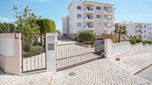 A gated residential complex with a paved entrance, a clear sky, and a multi-story building with balconies. - Apartment "Meia Praia Beach" with Sea View, Pool, Wi-Fi, Balcony & Garden (Lagos)