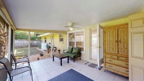 A covered patio with a ceiling fan, a green chair, a wooden table, and a large wooden cabinet. - Hidden gem close to everything!!! (Sarasota)