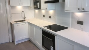 A modern kitchen with white cabinets, a stainless steel range hood, a built-in oven, and a dishwasher. - Newly refurbished, modern apartment in Hathersage, with parking (Hathersage)
