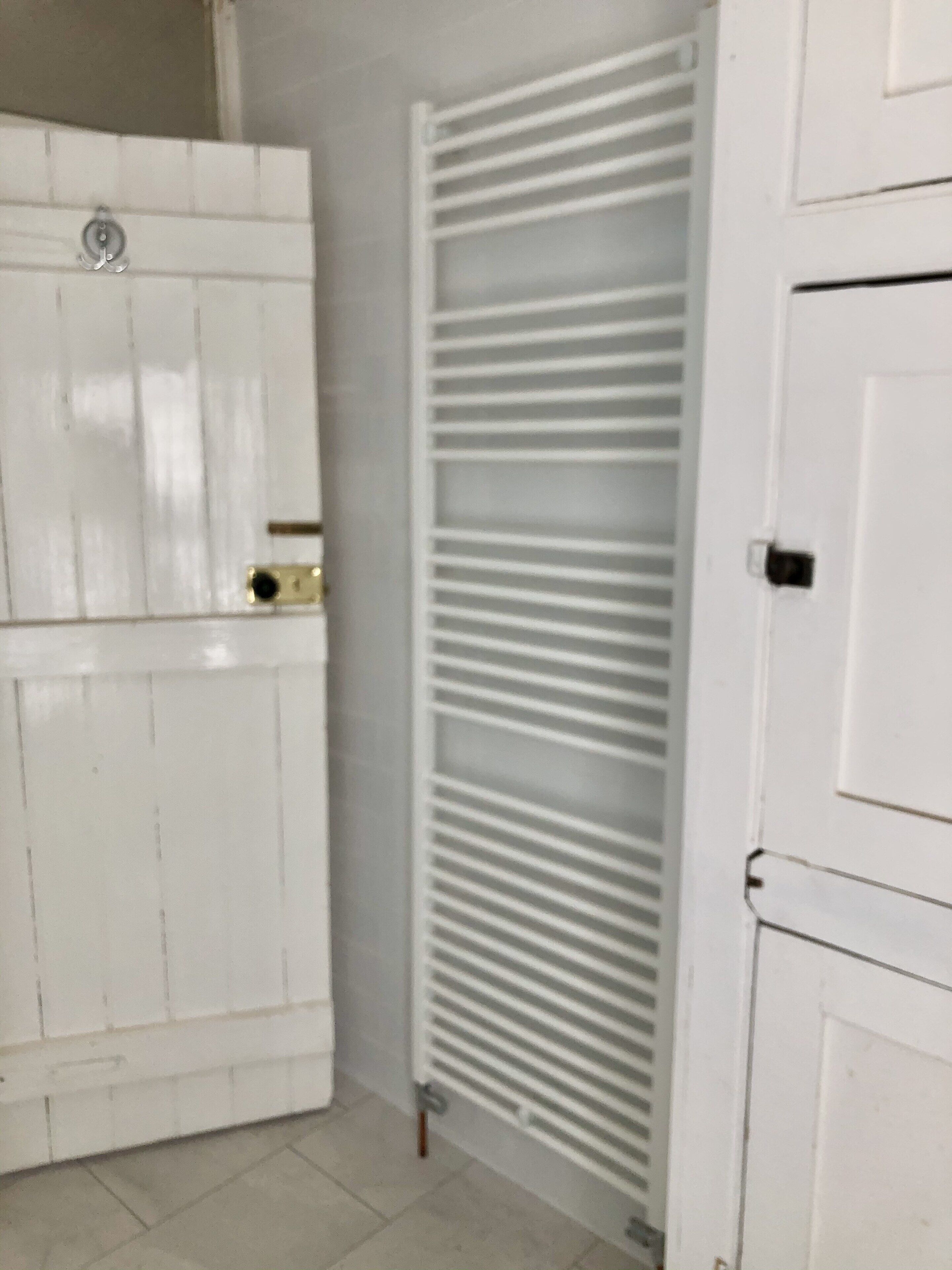 A white bathroom with a tiled floor, a white radiator, and a white door.