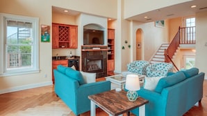 A spacious living room with a fireplace, a kitchen area with wooden cabinets, and a staircase leading to an upper level. - Triple Level House, Short Walk to Beach, Views, Multiple Balconies, Game Room, $300 in Free Tickets! (St. Augustine)