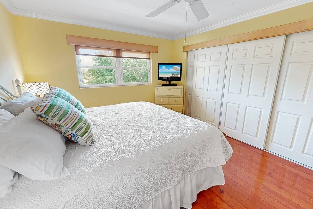 A bedroom with a bed, a television on a dresser, a window, and a set of white doors.