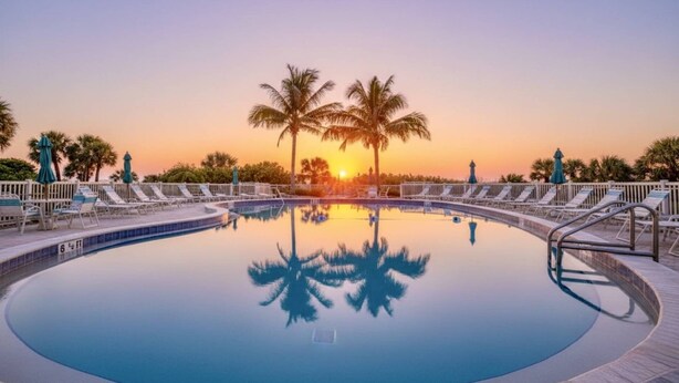 A circular pool with lounge chairs and palm trees, reflecting the sunset. - Private Beach | Bayside Corner Unit | Walk to Turtle Beach | 2 Heated Pools | Dog Friendly! (Sarasota)