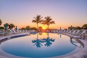 Ein kreisförmiger Pool mit Liegestühlen und Palmen, der den Sonnenuntergang spiegelt.
