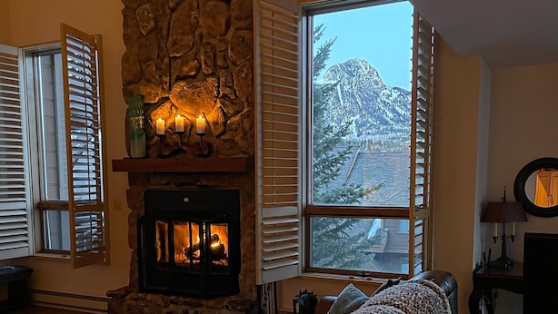 Un salon chaleureux avec une cheminée en pierre, un canapé en cuir et une grande fenêtre donnant sur les montagnes.