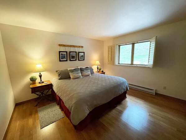 A bedroom with a bed, two bedside tables with lamps, a small rug, and a window with shutters. - Luxury, Mountain Views, Hot tub + Pool, 1 mile from Purgatory Ski Resort! (Durango)