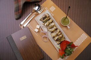 A neatly arranged meal with grilled chicken, a green sauce, and vegetables on a placemat, accompanied by cutlery and a napkin on a wooden table.