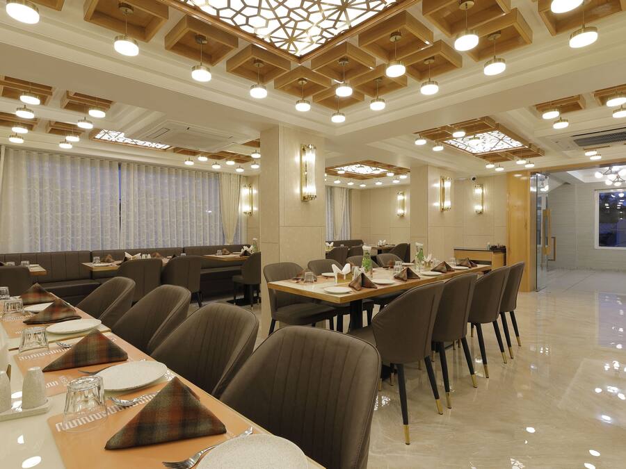 A modern dining area with multiple tables set for meals, a high ceiling with wooden beams, and a bright, well-lit ambiance.