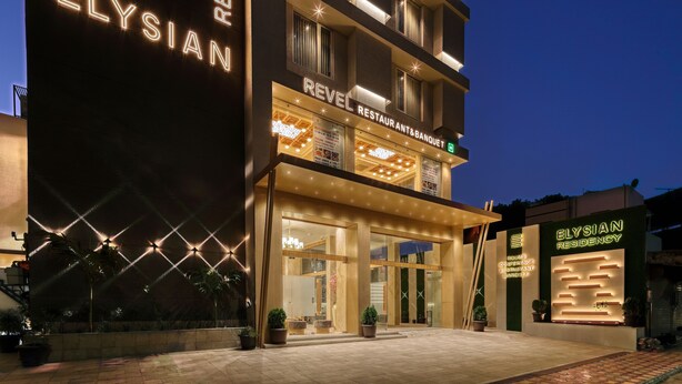 Un hotel con un llamativo letrero de 'Elysian Residency', un restaurante y salón de banquetes, y una entrada bien iluminada.