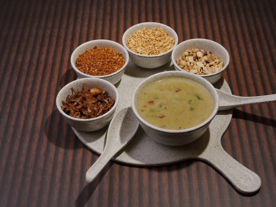 Una mesa con un tazón de sopa y cinco recipientes pequeños con distintos condimentos.