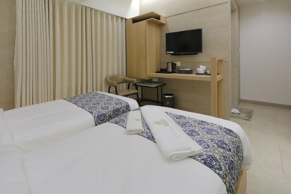 Habitación de hotel con dos camas, un escritorio, una silla, un televisor y un pequeño cubo de basura.