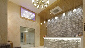 Un área de recepción con piso de mármol, un mostrador de recepción con pared de baldosas geométricas y una lámpara de araña moderna.