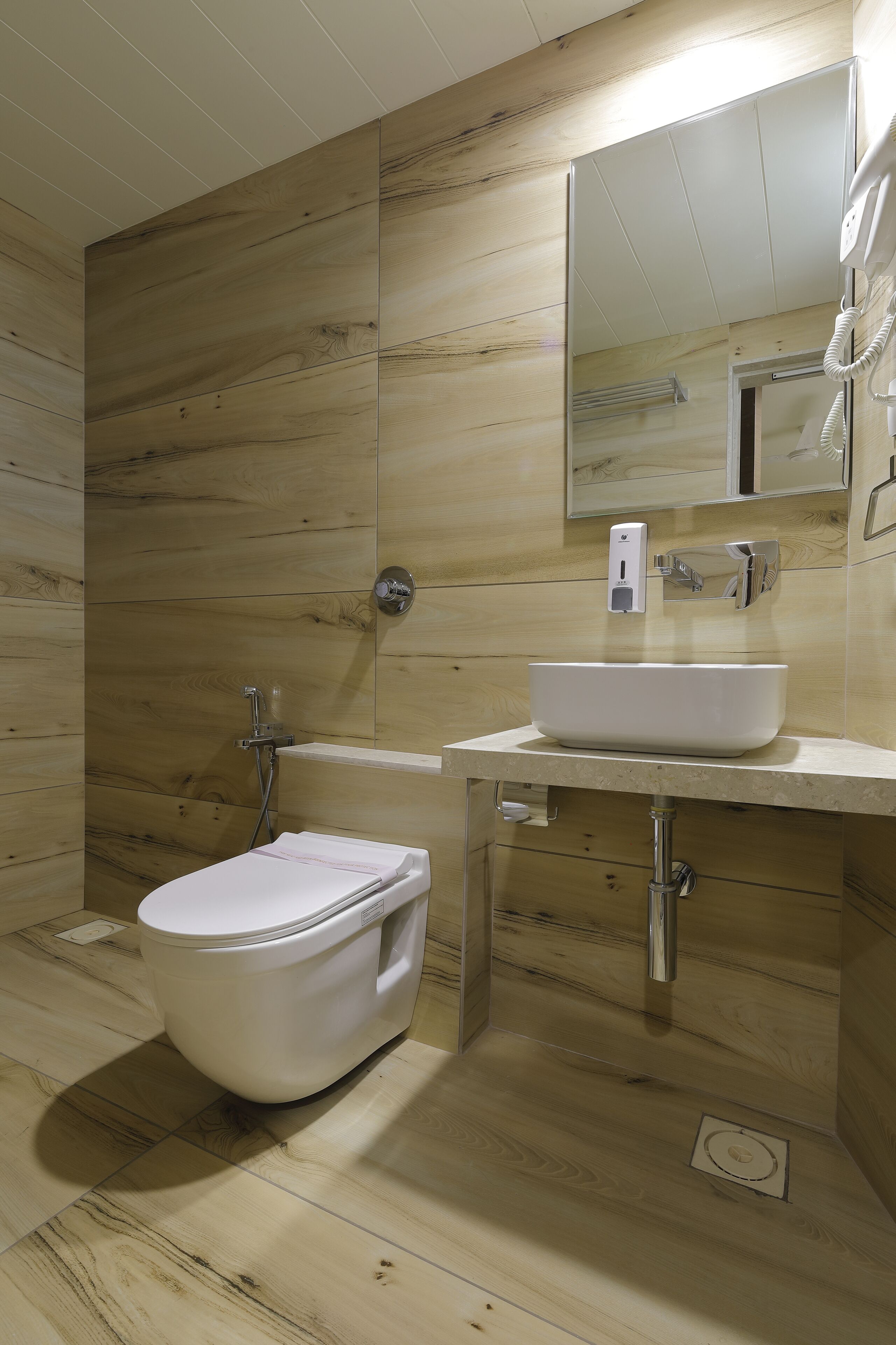 Un baño moderno con piso de madera, lavamanos blanco, espejo y retrete.