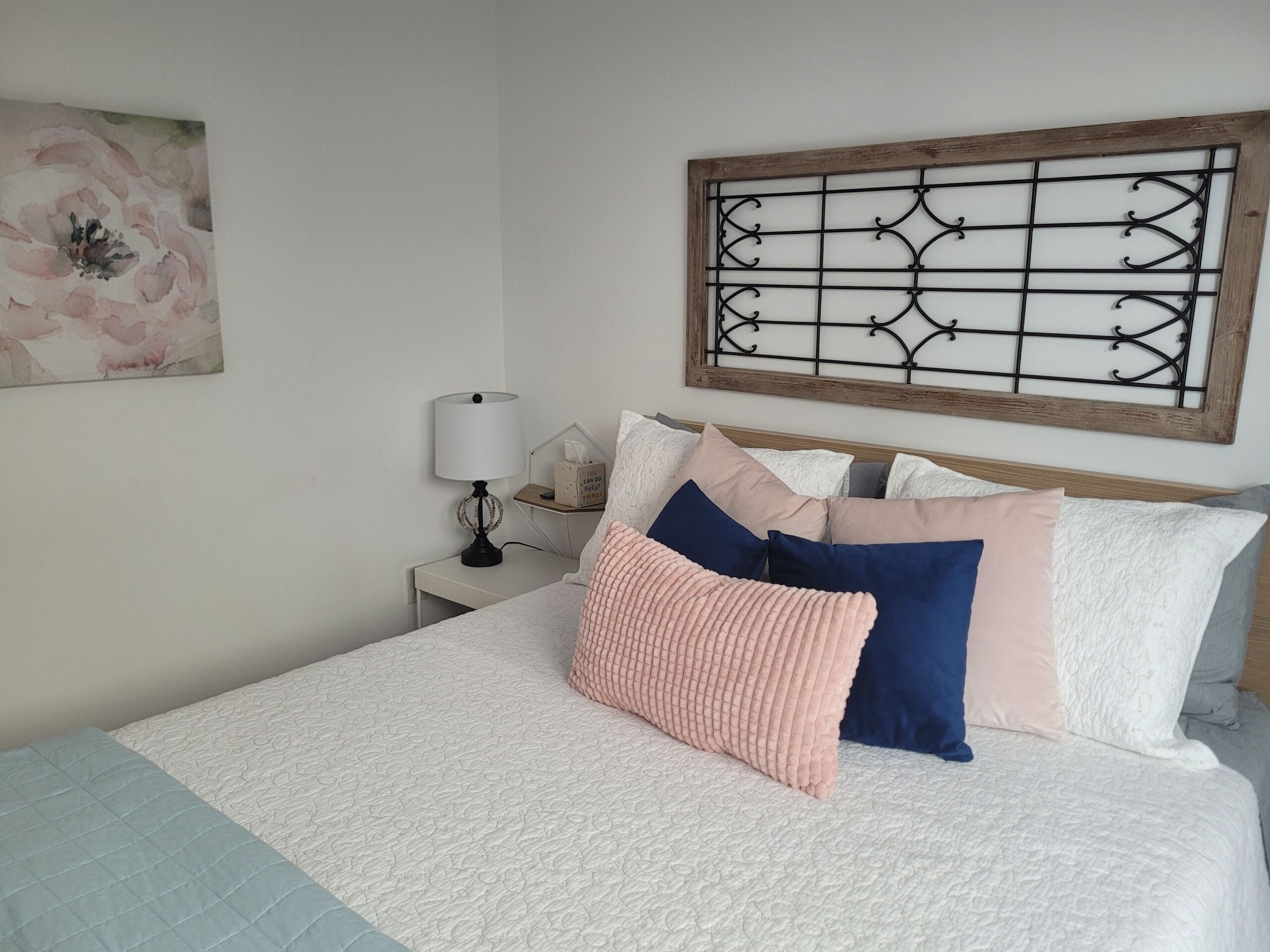 A neatly made bed with a white and light blue quilt, a wooden headboard, and a decorative metal panel above it.