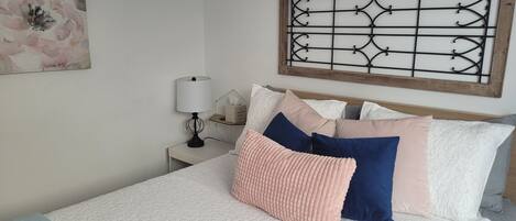 A neatly made bed with a white and light blue quilt, a wooden headboard, and a decorative metal panel above it.