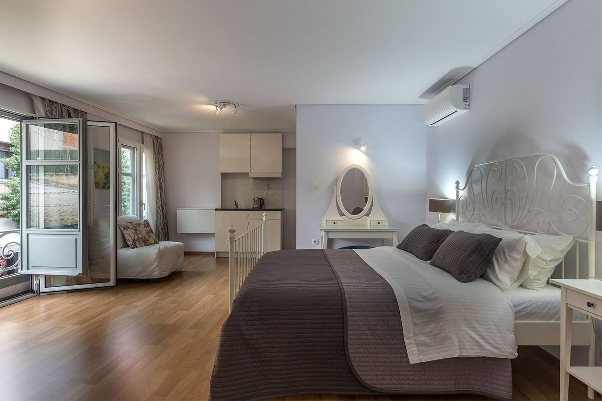 Quarto com cama, mesa de cabeceira, espelho e vista para o exterior.