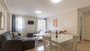 A modern living room with a grey sofa, a white dining table with chairs, and a TV mounted on the wall. - UrbanStay (Athens)