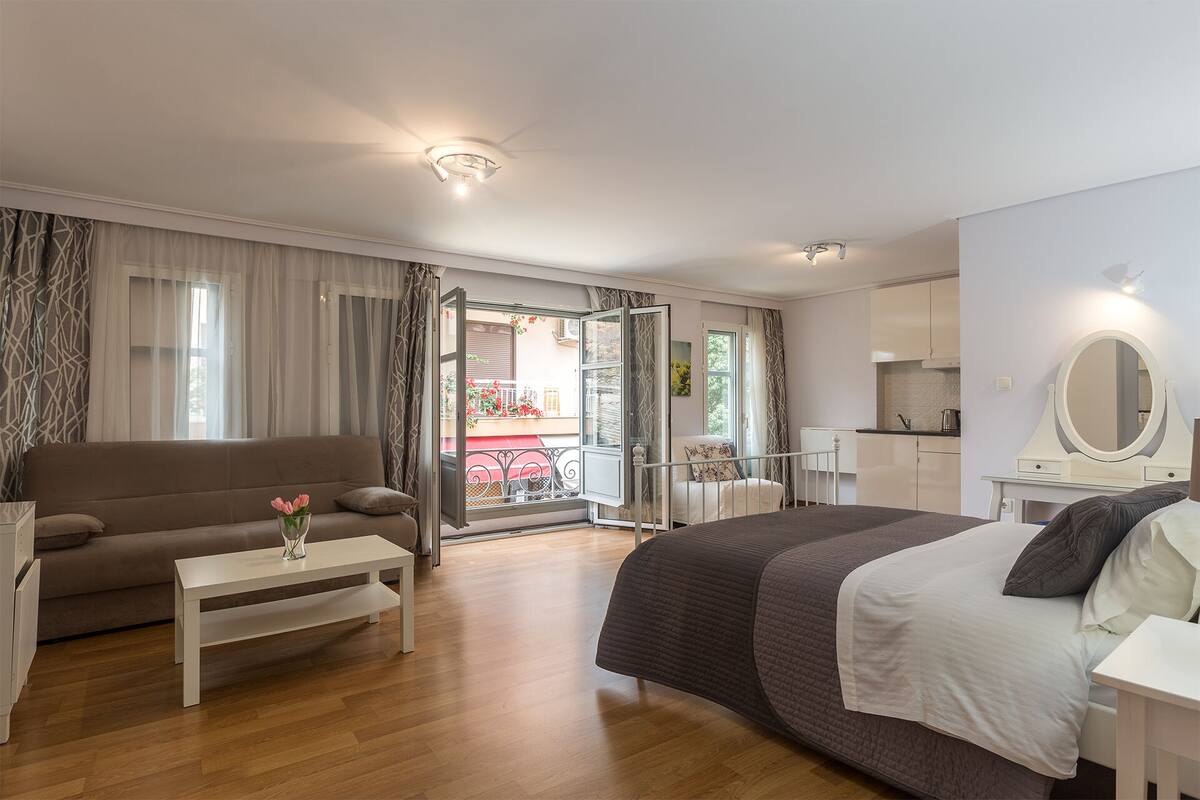 Quarto com cama, mesa de cabeceira, sofá e vista para uma varanda.