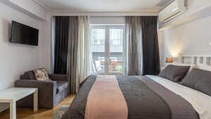 A hotel room with a large bed, a sofa, a TV, and a balcony with curtains. - UrbanStay (Athens)