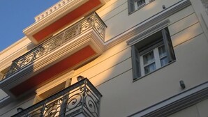 A multi-story building with a balcony featuring ornate metal railings and a red accent wall. - UrbanStay (Athens)