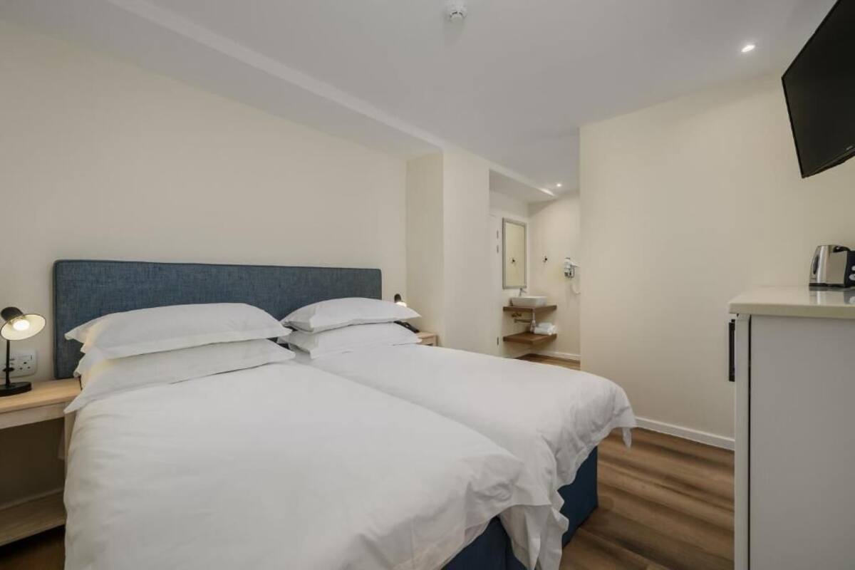 Ett hotellrum med två sängar, ett skrivbord, en platt-TV, ett handfat och ett litet kylskåp.