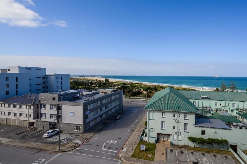Um hotel à beira-mar com estacionamento, uma estrada com placa de pare e vista para a praia e o oceano.