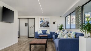 A modern living room with a blue sofa, a wooden coffee table, and a flat-screen TV mounted on the wall. - Paxton Luxury Apartments (Gqeberha (Port Elizabeth))