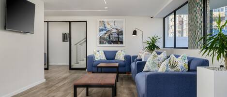 A modern living room with a blue sofa, a wooden coffee table, and a flat-screen TV mounted on the wall.