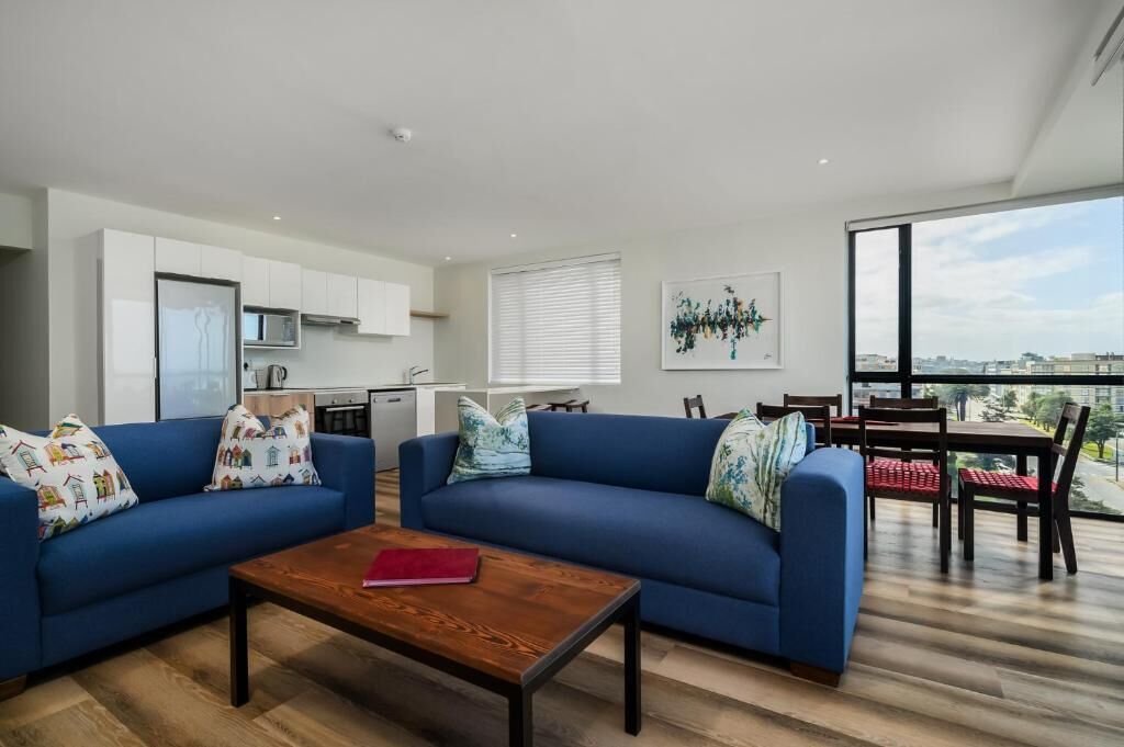 A modern living room with a blue sofa, a wooden coffee table, and a dining area with a table and chairs.