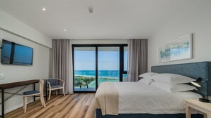 A hotel room with a large bed, a desk with a chair, a TV, and a view of the ocean. - Paxton Luxury Apartments (Gqeberha (Port Elizabeth))
