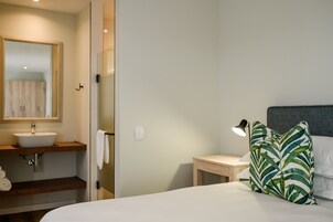 A hotel room with a bed, a nightstand, a bedside lamp, a wooden nightstand, a white sink, a mirror, and a towel rack.