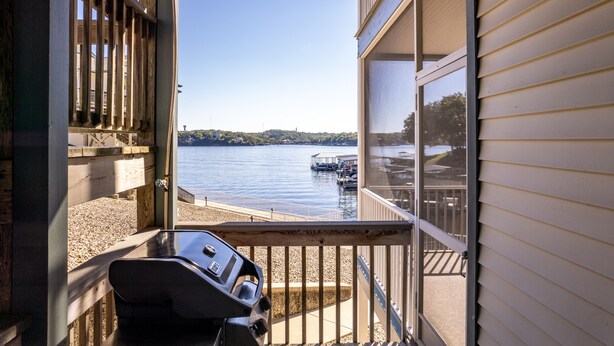 A balcony with a grill, overlooking a lake with docks and boats. - Evergreen 209 - Lower Level 3 Bdrm Lakefront Condo (Sunrise Beach)