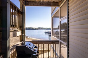 A balcony with a grill, overlooking a lake with docks and boats.