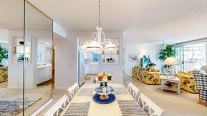 Una sala de estar moderna con comedor, muebles blancos y un ventanal que proporciona luz natural.