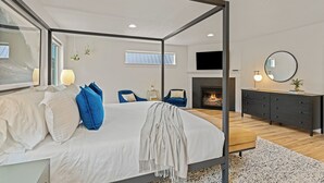 Ein modernes Schlafzimmer mit Himmelbett, Kamin, Fernseher und einem großen Spiegel.