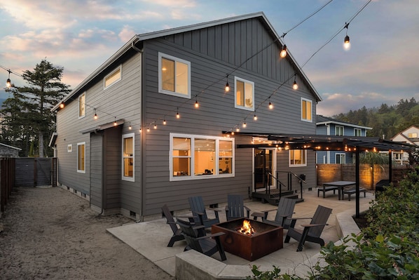 A two-story house with a covered patio area, outdoor seating, and a fire pit.
