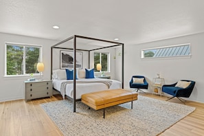 A bedroom with a four-poster bed, a wooden bench, two chairs, a bedside table, and a nightstand.