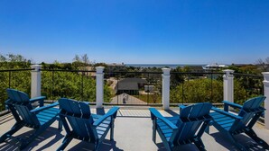 Un balcon avec des chaises bleues et une vue dégagée sur l’océan et les maisons environnantes.