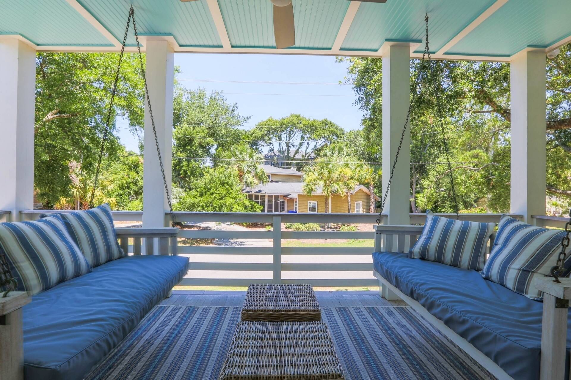 Une véranda couverte avec deux coins salon dotés de coussins bleus et d’un pouf en osier.