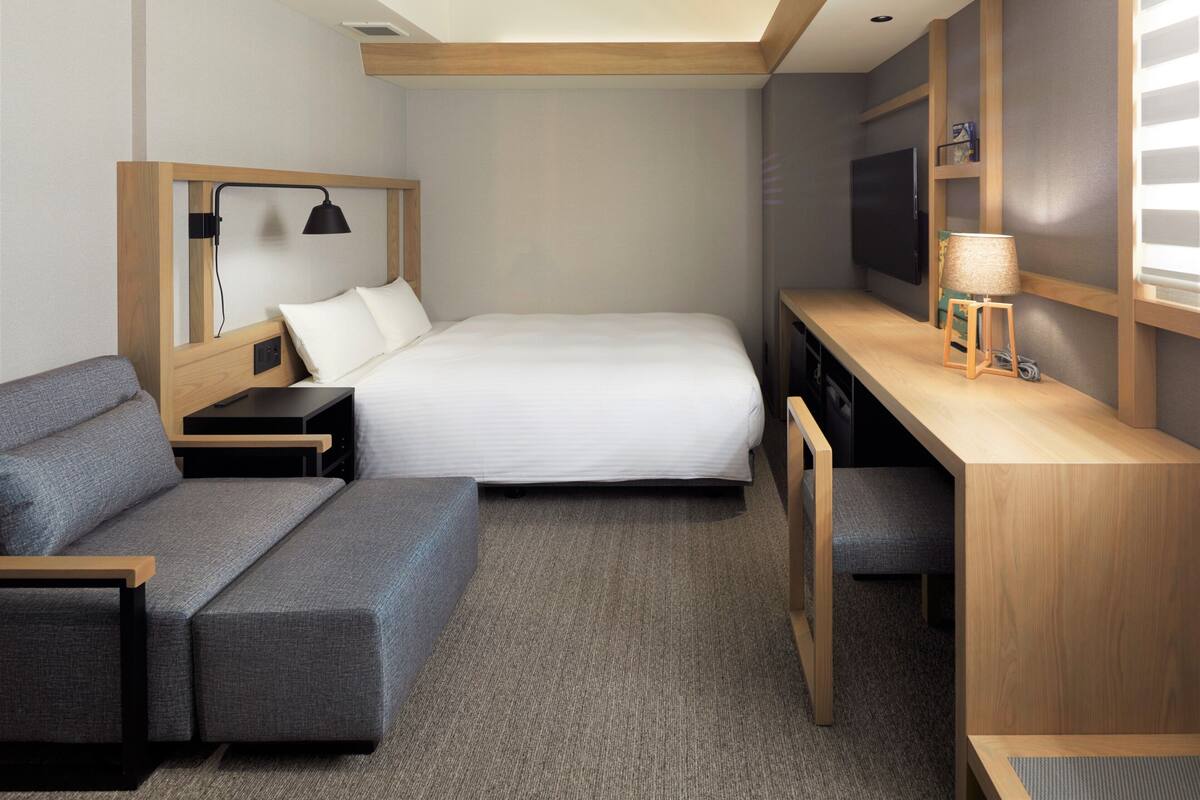 A compact hotel room with a bed, a sofa, a desk, and a TV.