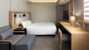 Una habitación de hotel compacta con una cama, un sofá, un escritorio y un televisor.