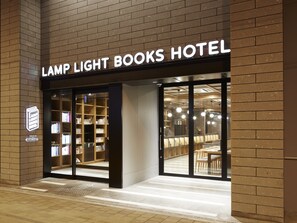 The exterior of the Lamp Light Books Hotel with a brick facade, large glass entrance, and a visible seating area inside. - Lamp Light Books Hotel Sapporo (Sapporo)