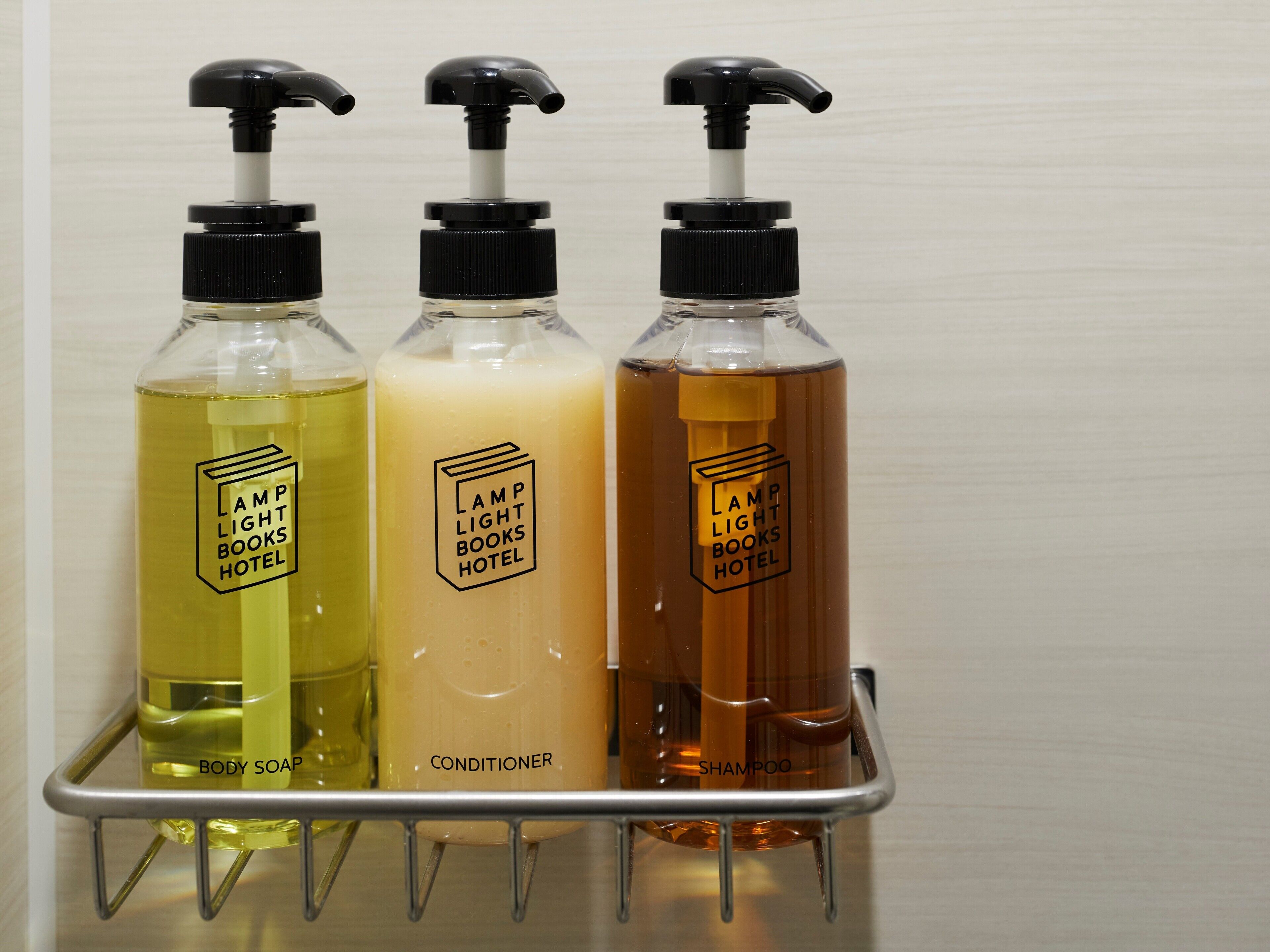 Three bottles of body soap, conditioner, and shampoo on a metal rack.