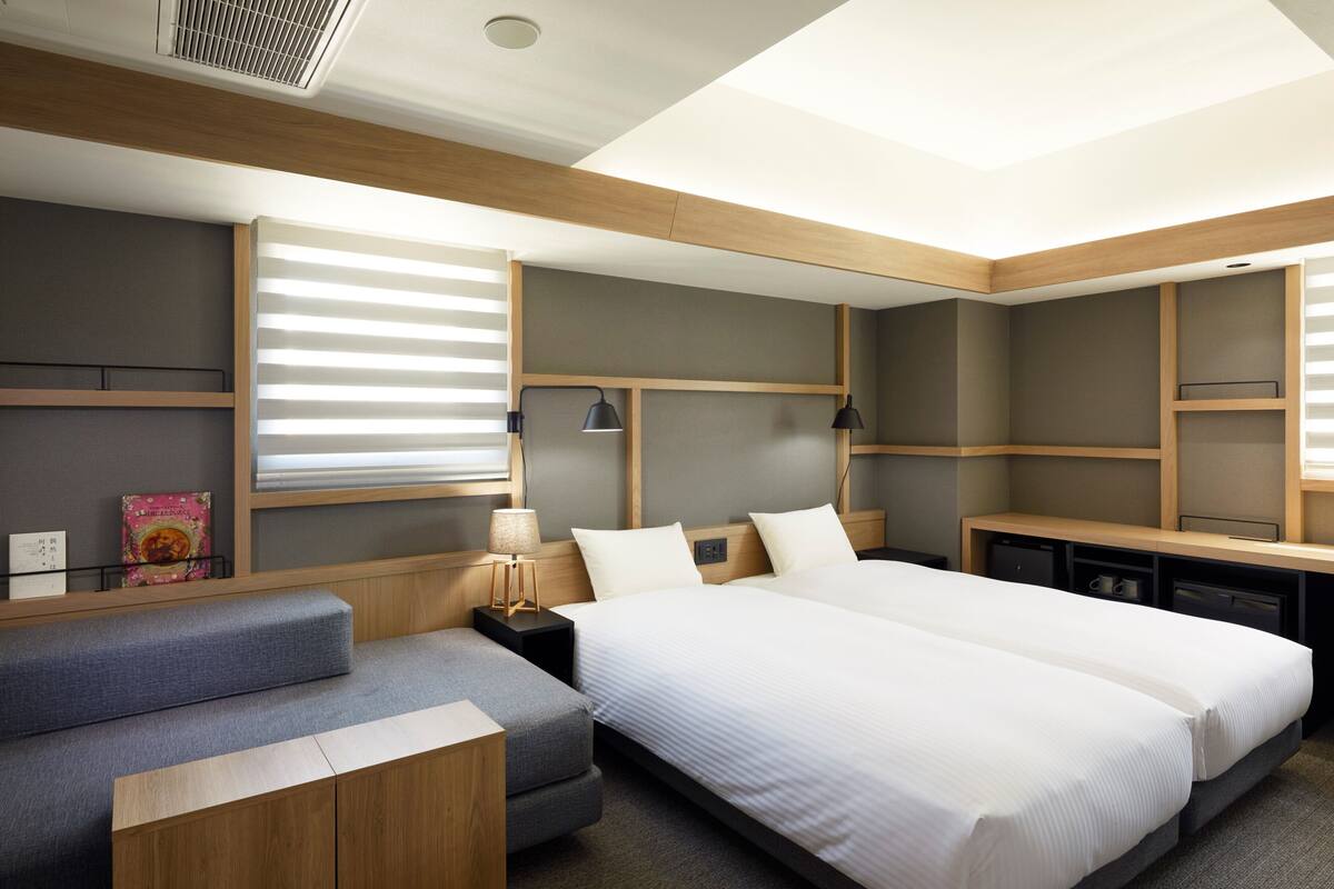A modern hotel room with a large bed, a sofa, a desk, and a lamp.