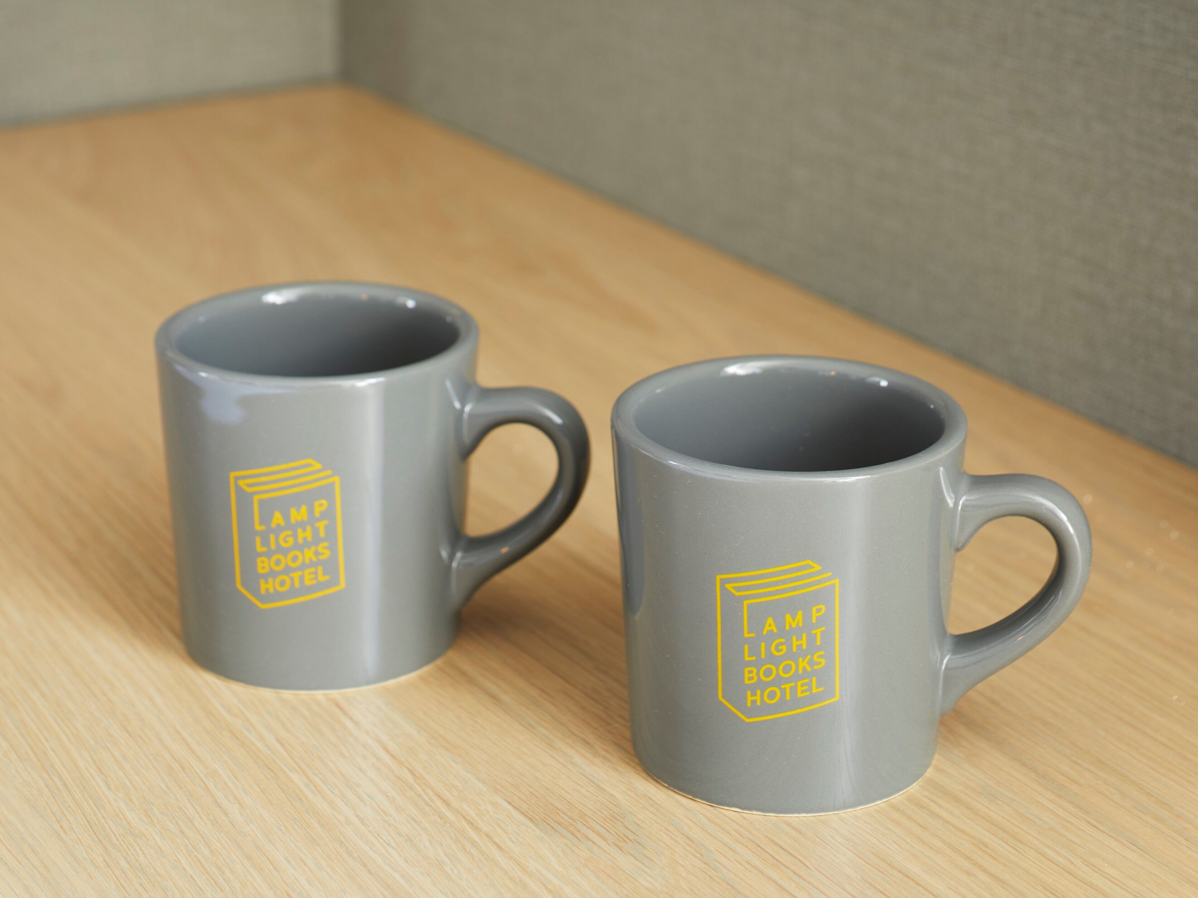 Duas canecas cinzas com um logotipo amarelo sobre uma superfície de madeira.