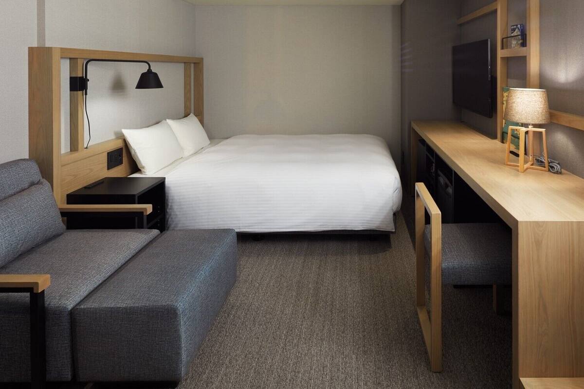A compact hotel room with a bed, a desk, a chair, a sofa, and a TV.
