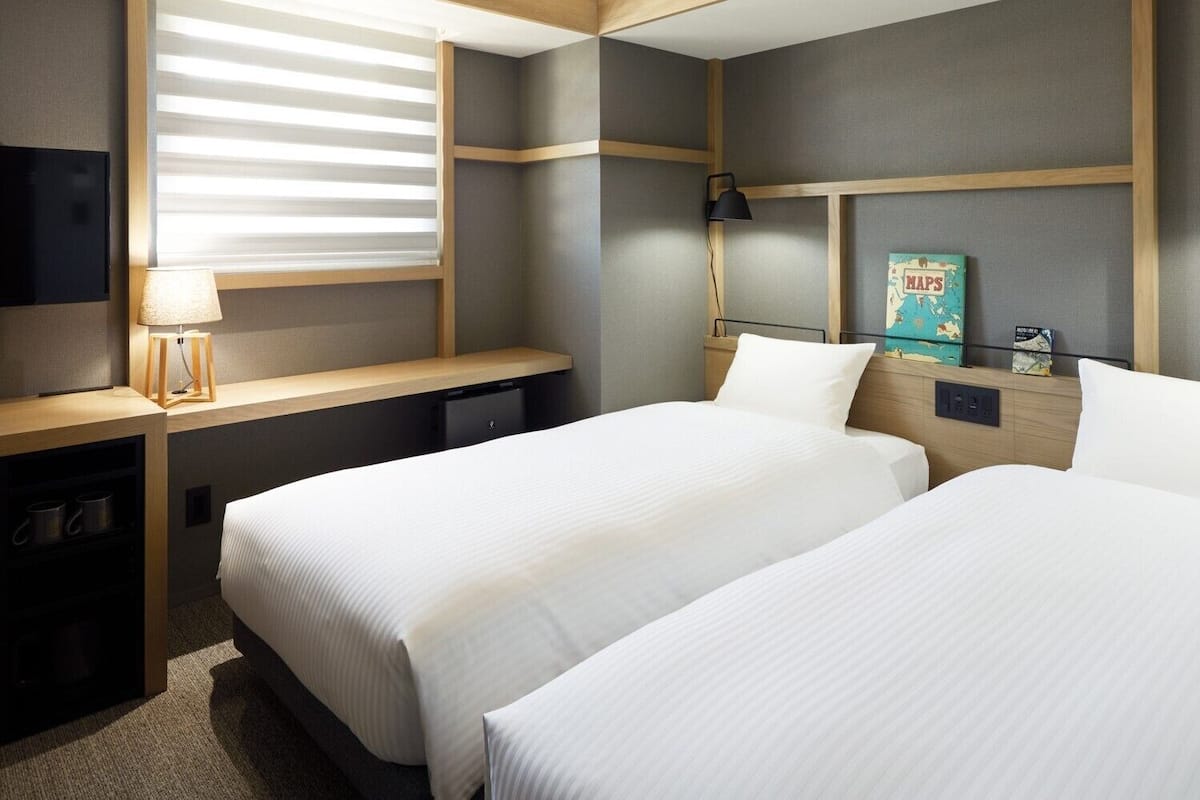 Habitación de hotel con dos camas, un escritorio, una lámpara, un televisor y un cuadro con un mapa en la pared.