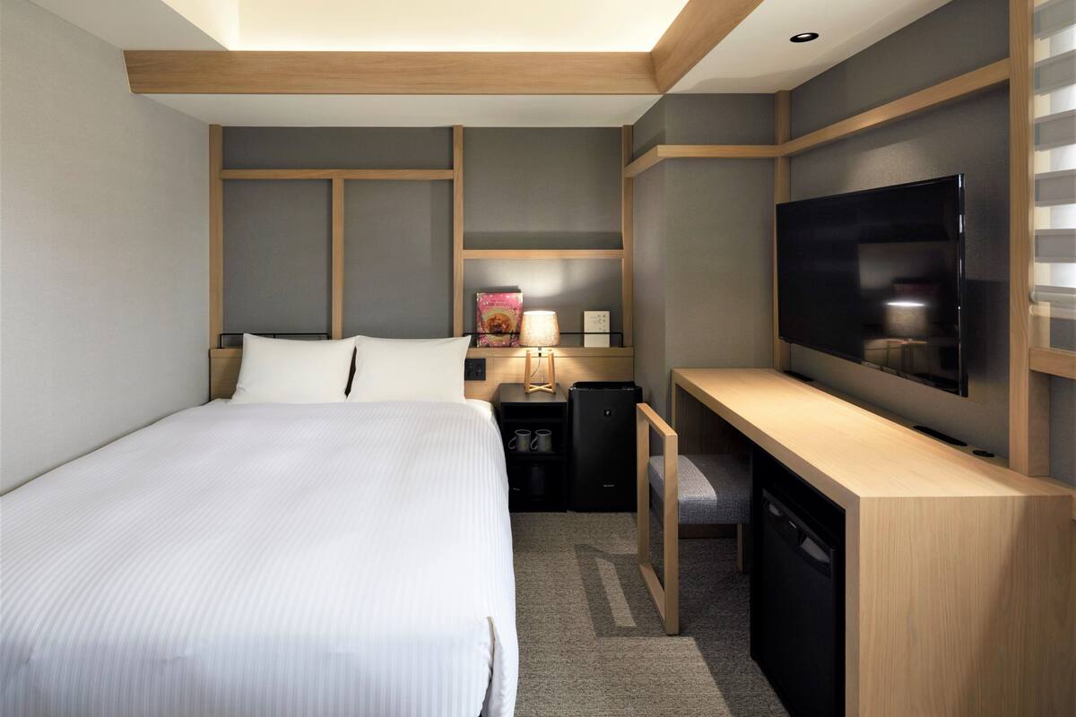 A hotel room with a bed, a desk, a television, and a small table with a lamp.