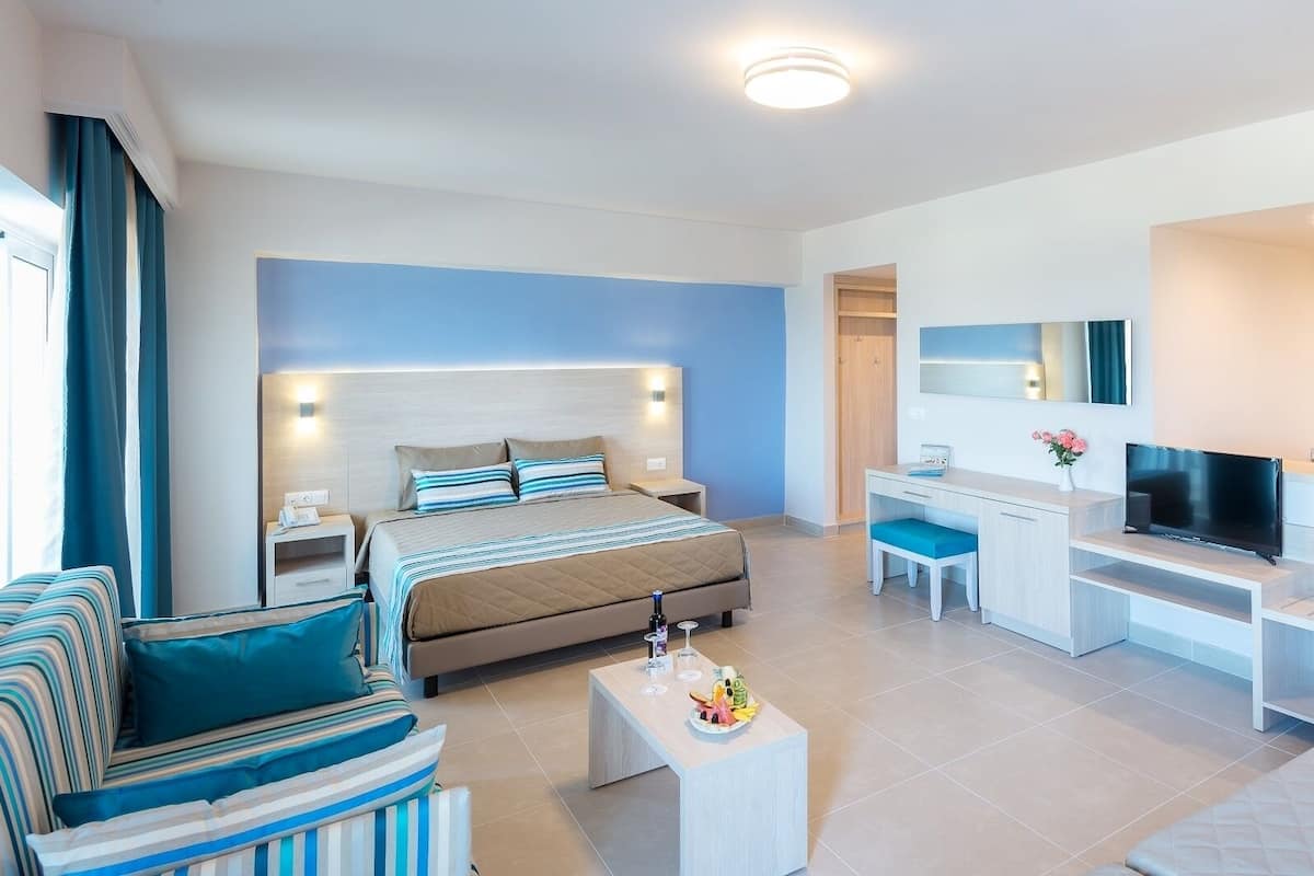 A modern hotel room with a bed, a desk, a TV, and a kitchenette.